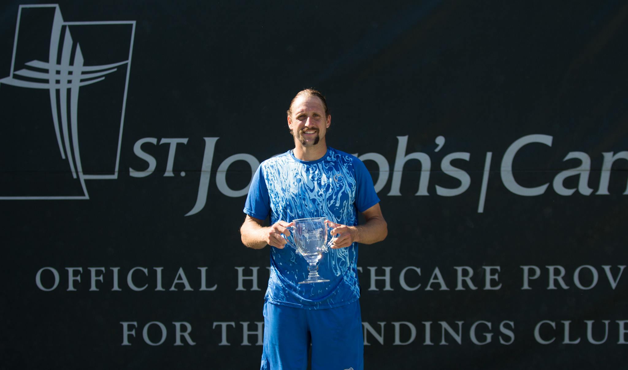 A male tennis player holds his crystal trophy after winning at the Savannah Challenger tennis tournament.