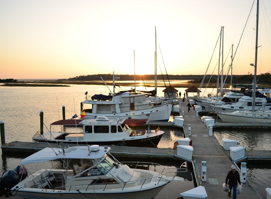 The sun sets on several boats docked at one of the well-kept marinas on the coast.