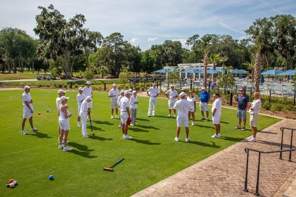 Residents wearing all white gather on the lawn to prepare for a game of croquet.