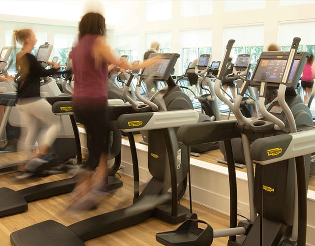 Two women wearing workout apparel use the elliptical machines at the wellness center.