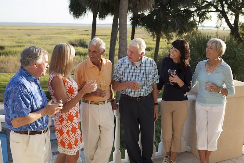 Six neighbors stand and chat in front of palm trees while enjoying beverages on a seasonal evening at The Landings.