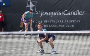 A male tennis player crouches at the net while his partner returns a serve during the Savannah Challenger tennis tournament.