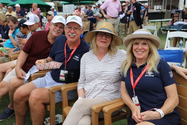 Two men and two women pose for a photo while seated and watching the Club Car Golf Championship.