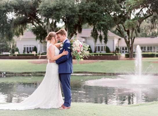Bride and groom embrace in front of a tranquil pond at their unique wedding venue.