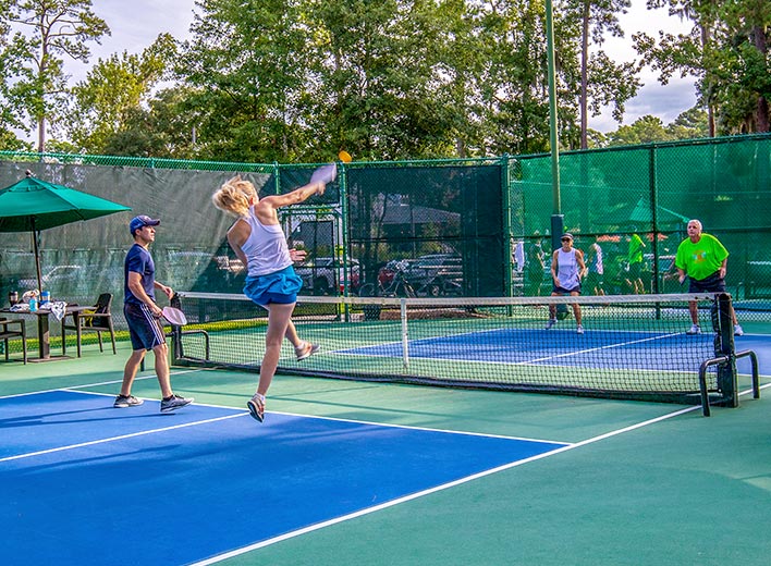 A woman pickleball player returns a serve as her male teammate watches during a match with another couple on one of The Landings' many courts.