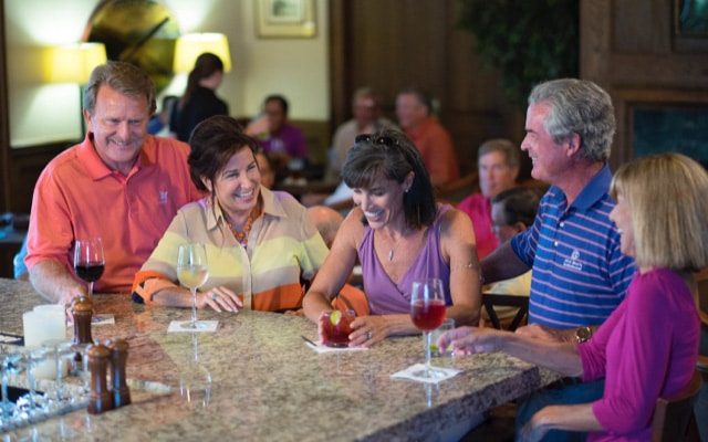 Five neighbors meet and laugh over drinks at the bar while enjoying the bustling clubhouse scene.