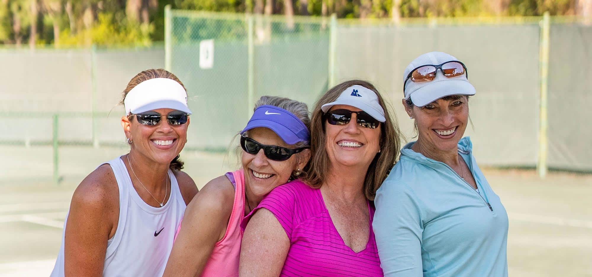 Four female neighbors and friends, wearing hats and visors, enjoy a sunny day playing court sports at The Landings.