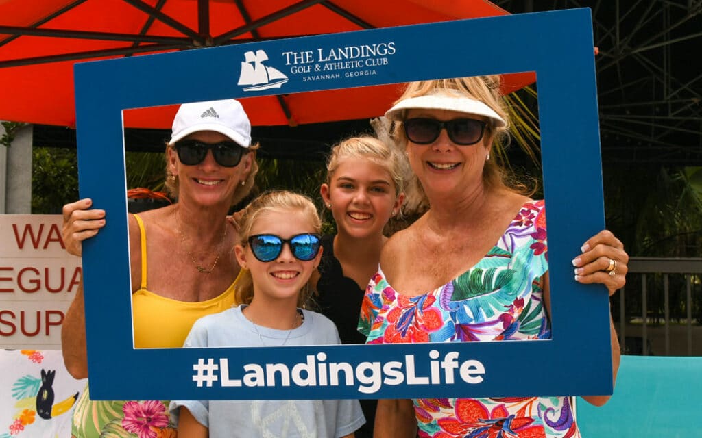 Multiple generations of women posing for a photo opportunity with a #LandingsLife frame as members of the Athletic Club.