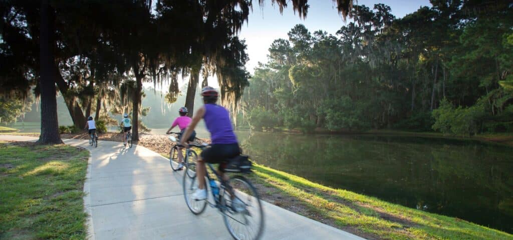 Family of four riding their bicycles along a paved path next to a pristine lagoon. at sunset.