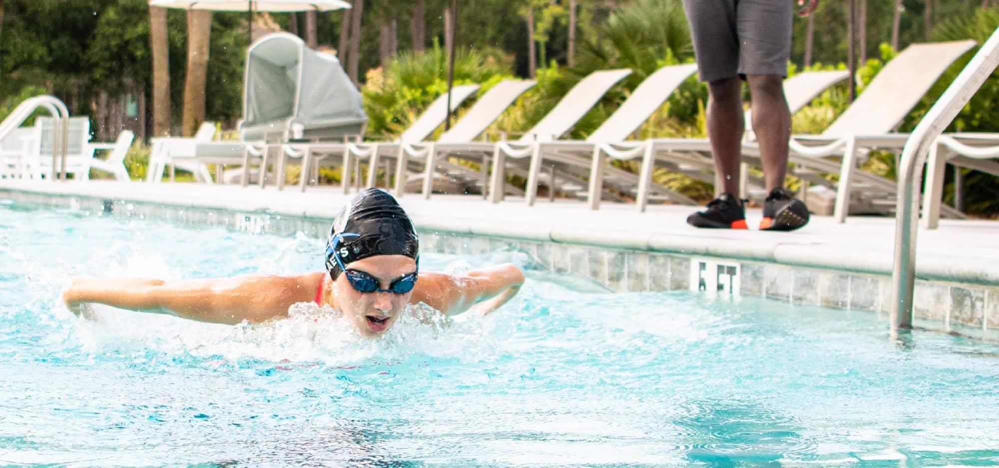 Swimmer wearing a swim cap and goggles does the butterfly stroke while doing laps in one of the five pools.