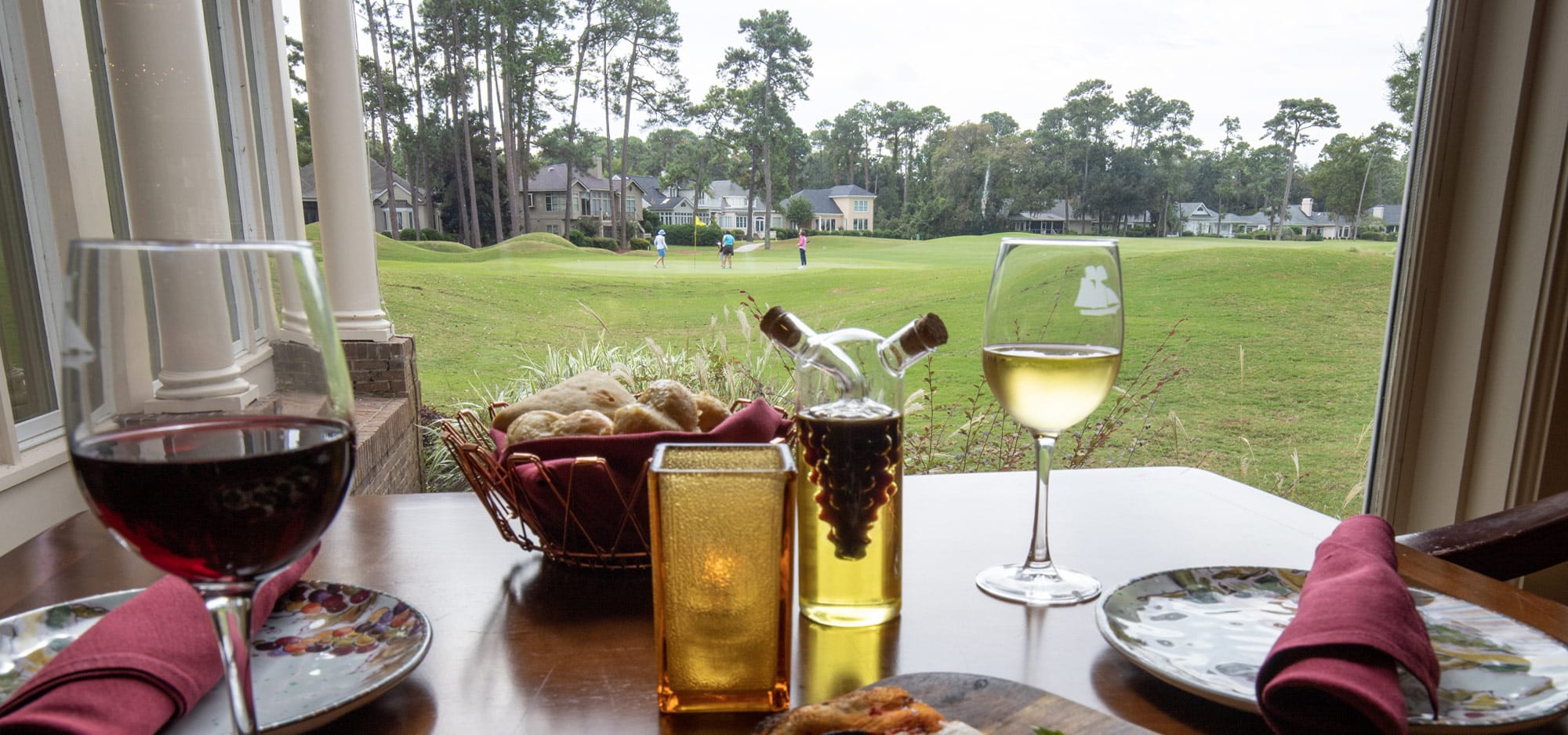 A glass of red wine, basket of bread and a glass of white wine sit on a restaurant table that has a view of golfers playing a round on one of the six championship courses.