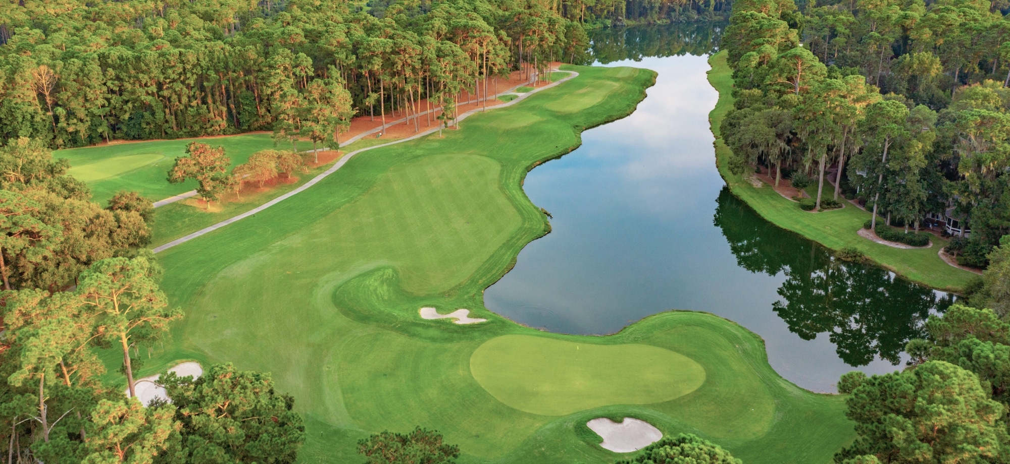 An aerial view of Deer Creek golf course hole #5 lined with trees and a lagoon.